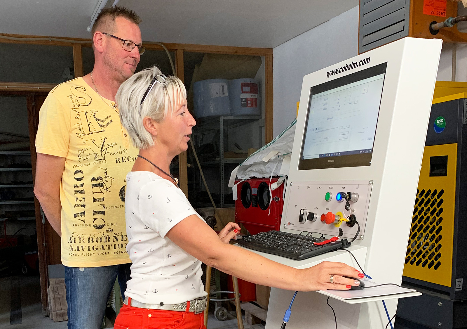 Eine Frau steht an einem Computer und überwacht die Steuerung einer Steinbearbeitungsmaschine, ein Mann schaut zu.