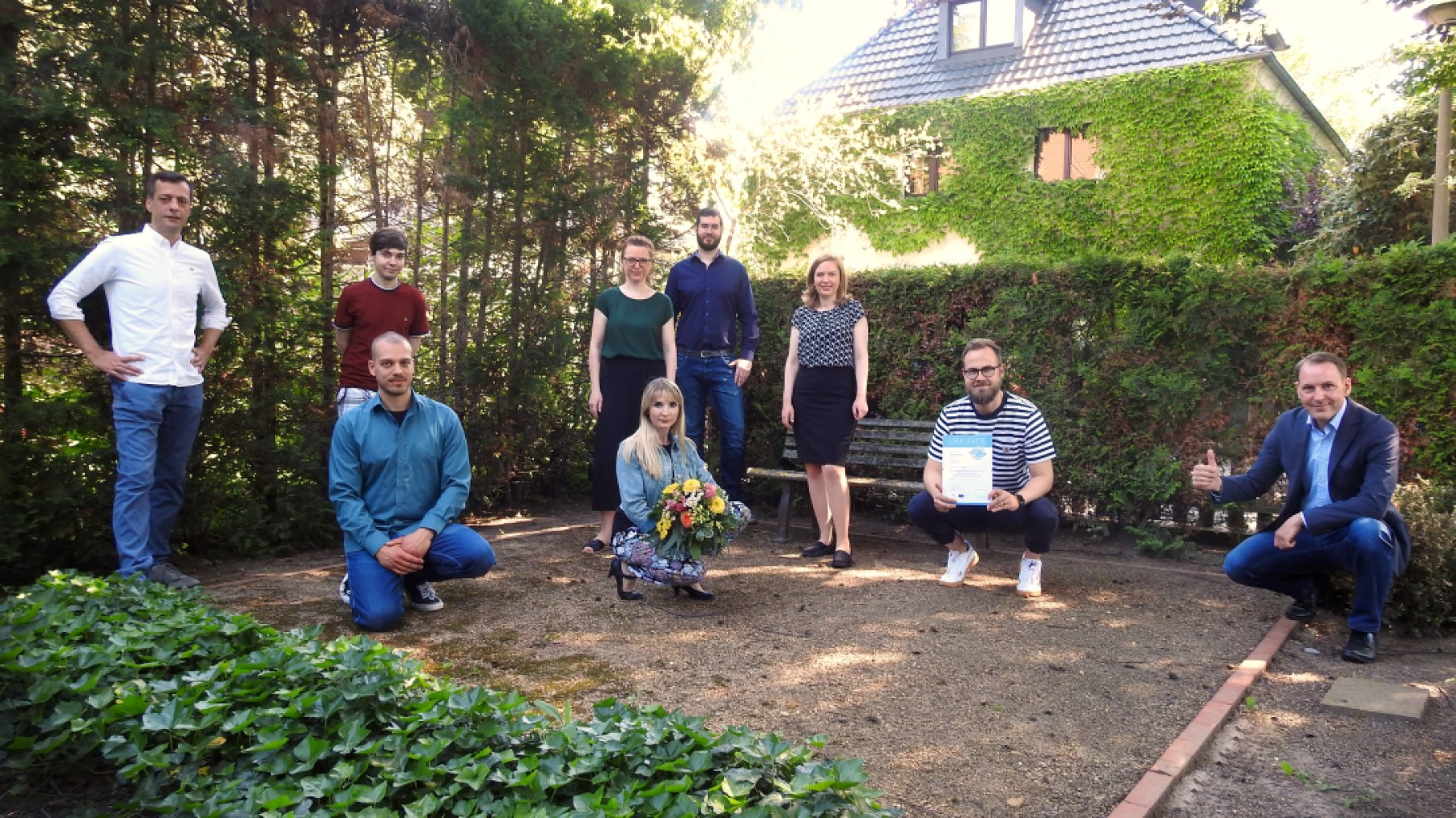 Regionalberater Norbert Köhn überreicht dem Team von DEVDEER GmbH die Urkunde und einen Blumenstrauß