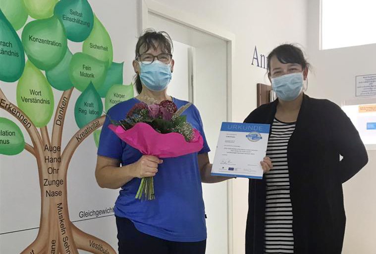 Regionalberaterin Claudia Berge überreicht Praxisinhaberin Urkunde und Blumen