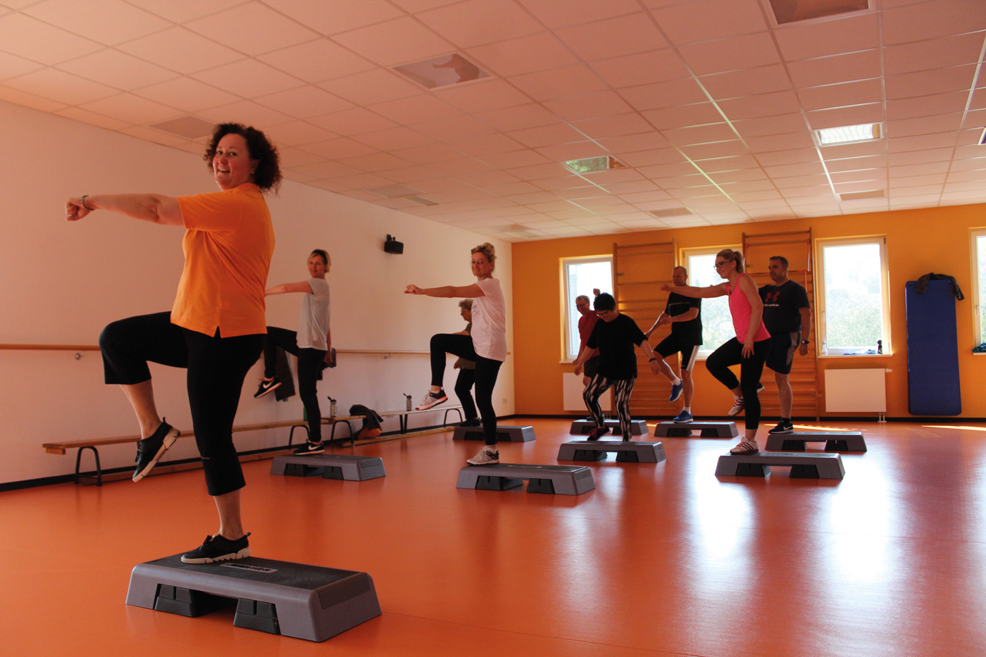 Eine Gruppe Männer und Frauen schauen nach vorne und machen Step-Aerobic