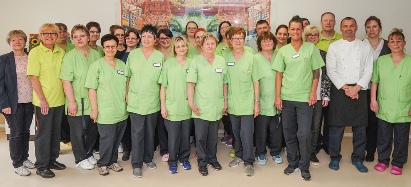 Die Mitarbeiterinnen und Mitarbeiter stehen zusammen und blicken nach vorne in die Kamera