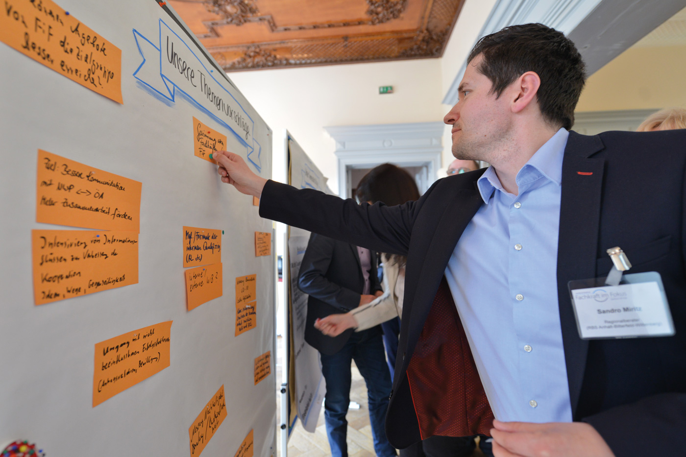 Ein Mann im Anzug heftet beschriebene Karten an eine Pinnwand