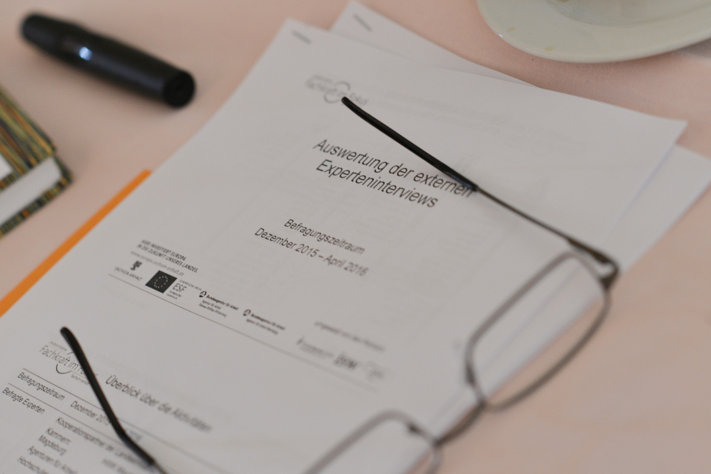 Ein Papierausdruck einer Präsentation, darauf steht Auswertung der externen Experteninterviews,auf dem Papier liegt eine Brille