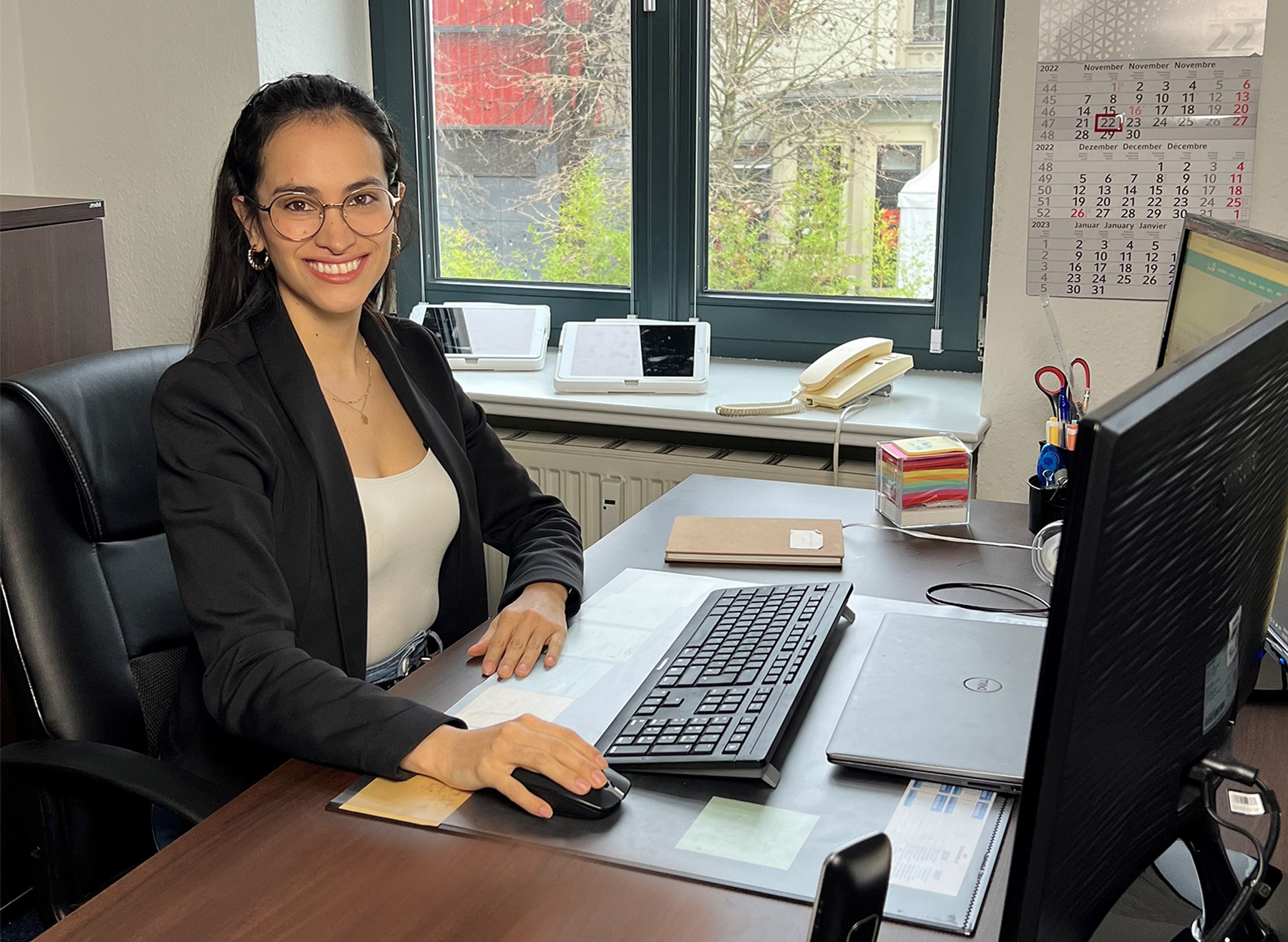 Eine junge Frau sitzt sehr gut gelaunt an einem Computerarbeitsplatz