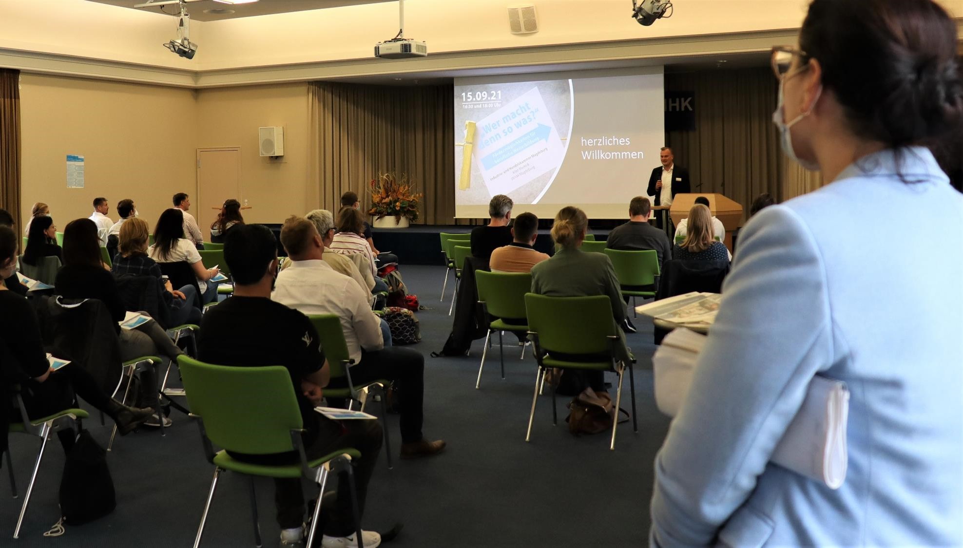 Mann auf der Bühne begrüßt Teilnehmer