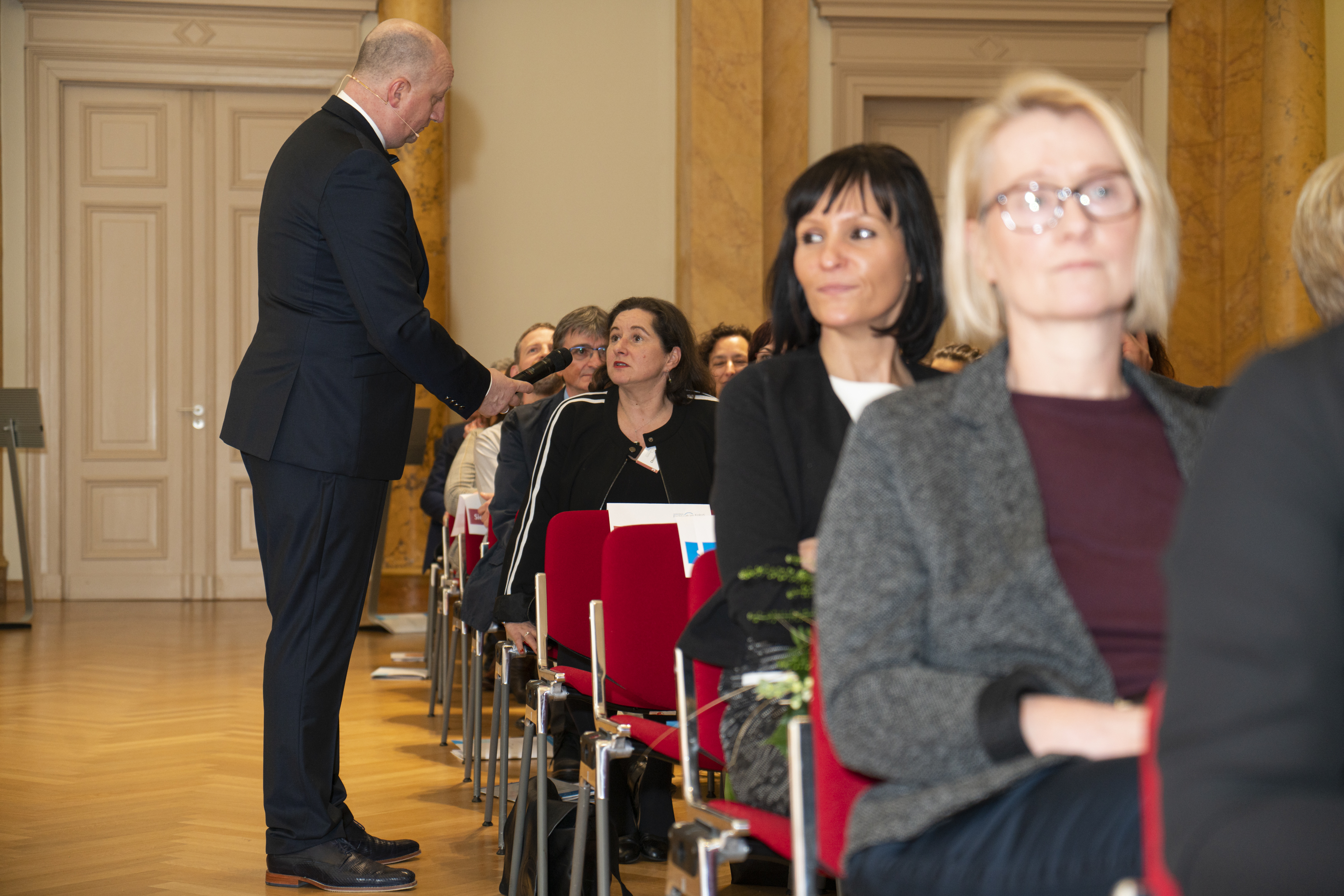 Ein Mann steht neben jemanden der sitz und hält ein Mikrofon hin