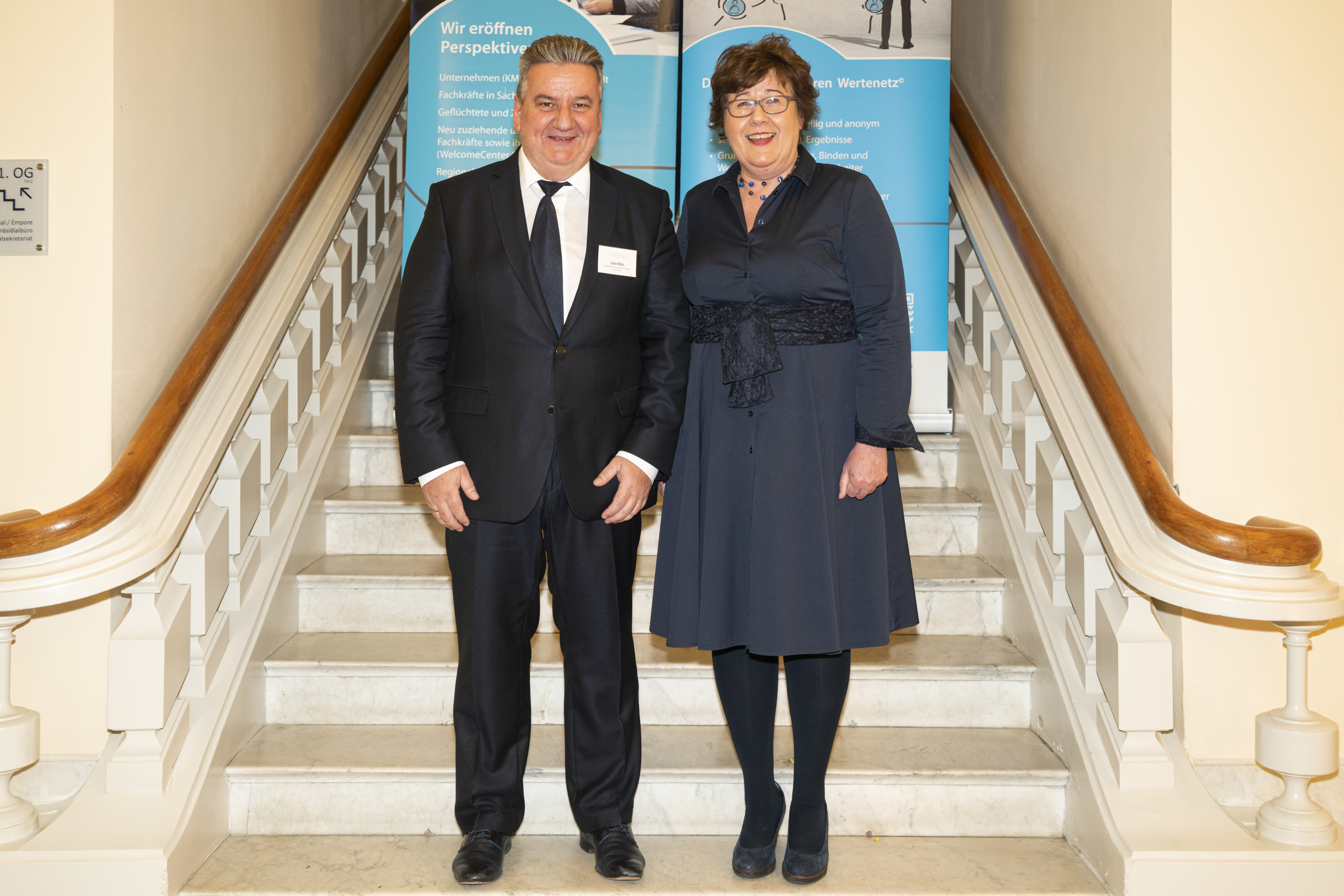 Ein Mann steht neben einer Frau auf der Treppe, sie schauen in die Kamera