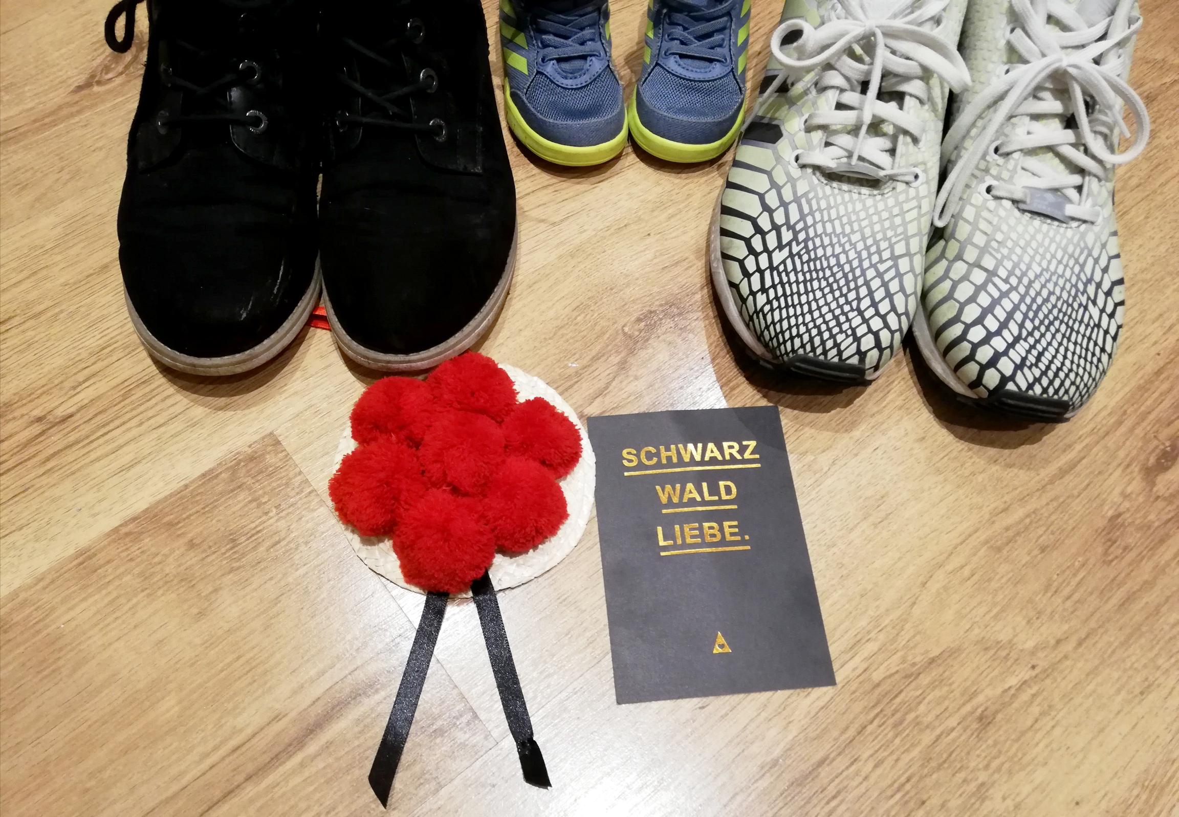 Blick von oben auf 3 Paar Schuhe, darunter ei Paar Kinderschuhe, ein kleiner Schwarzwald hut und einer Postkarte auf der Schwarzwaldliebe steht
