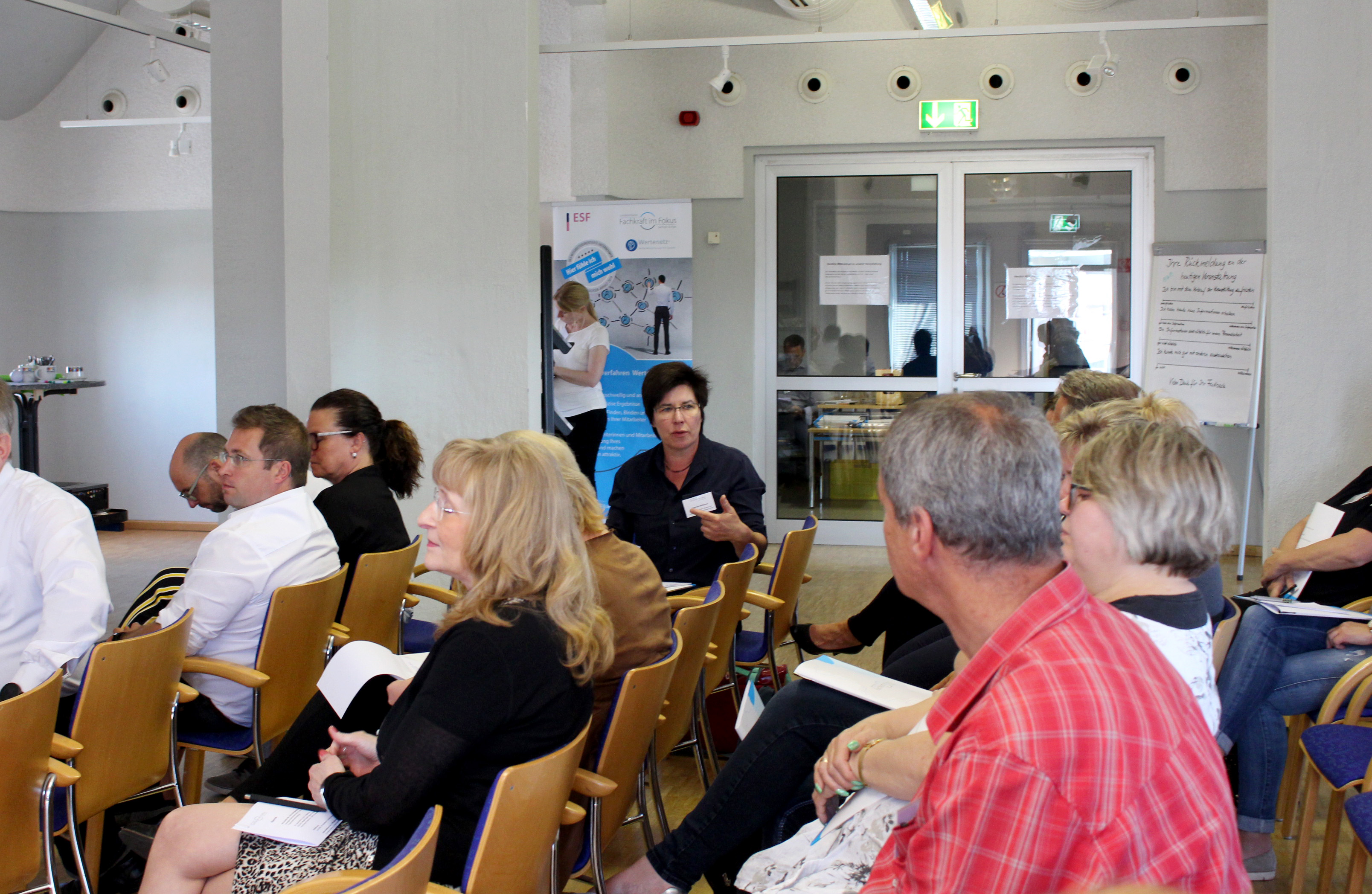 Viele Menschen sitzen in einem Raum, wo ein Vortrag statt findet.