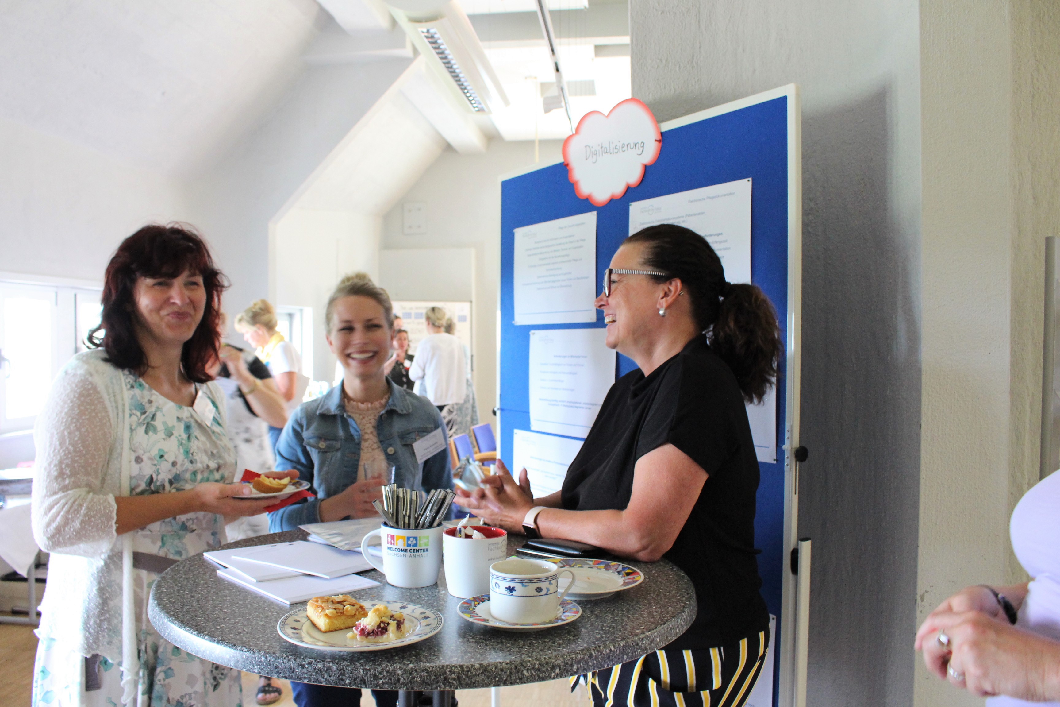 Frauen stehen vor einer Informationstafel und lachen.
