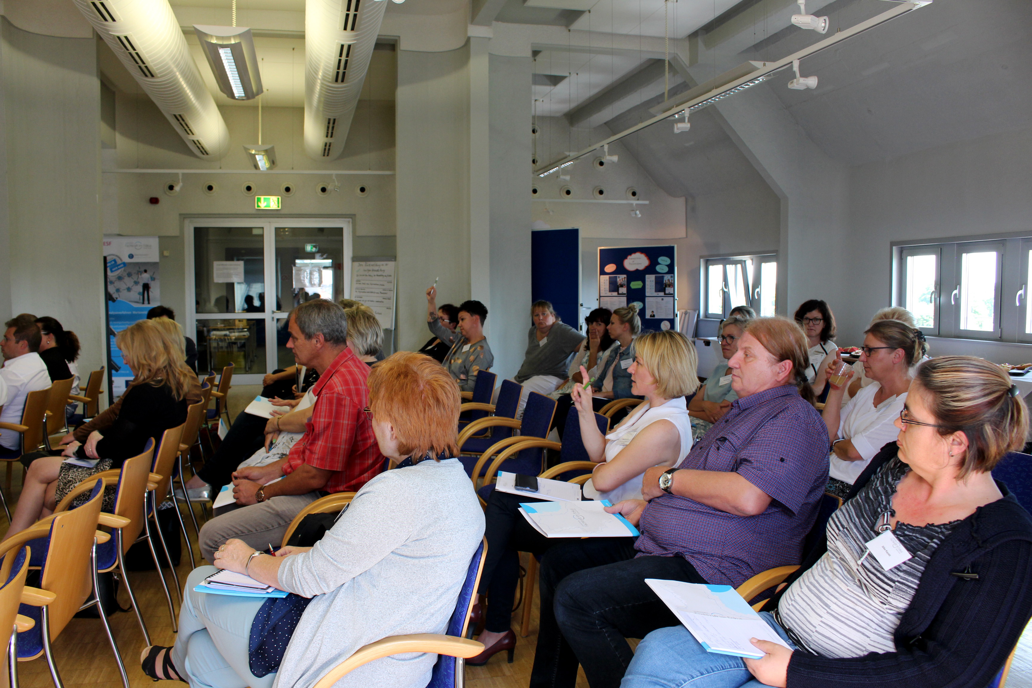 Viele Menschen sitzen in einem Raum, wo ein Vortrag statt findet.