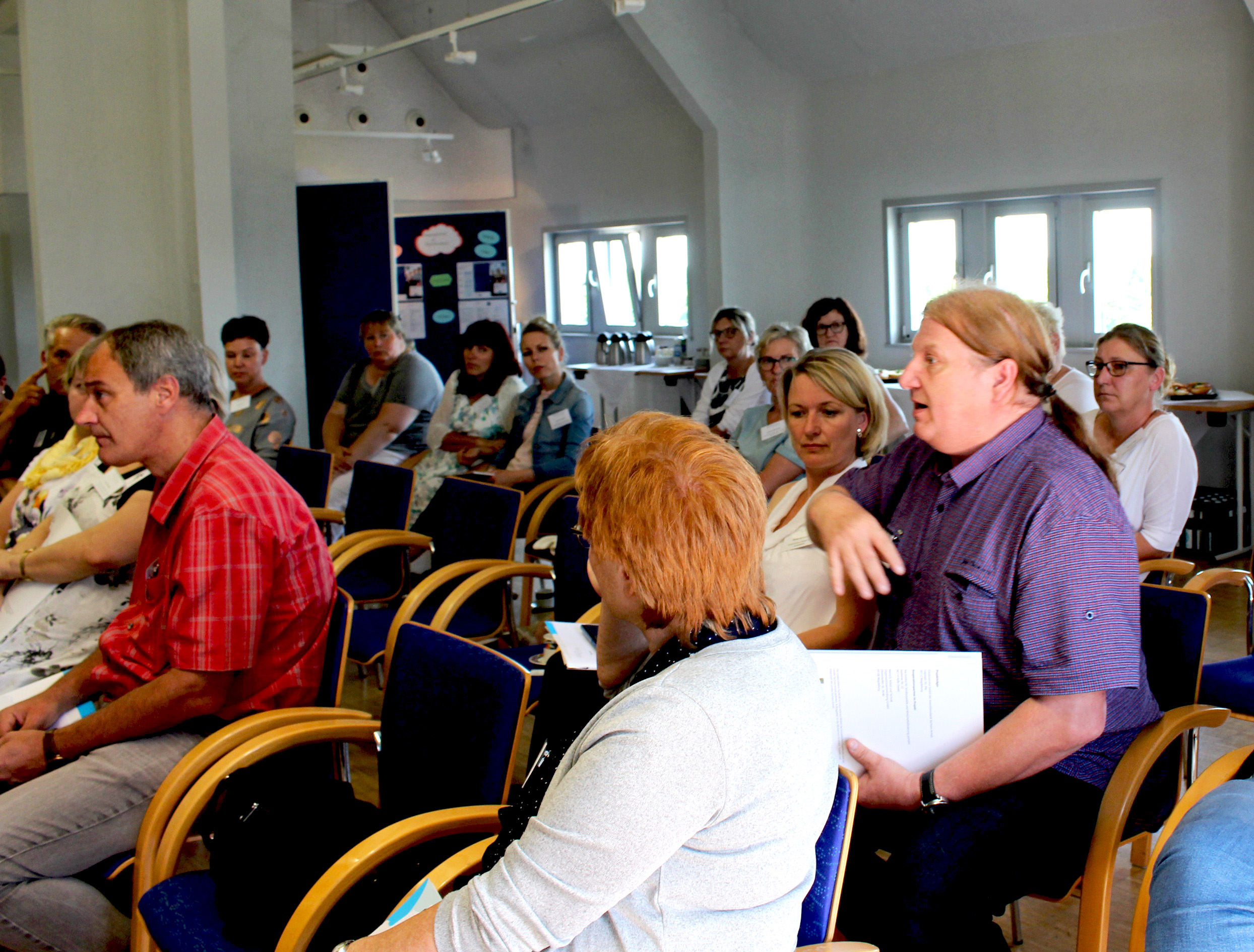 Viele Menschen sitzen in einem Raum, wo ein Vortrag statt findet.