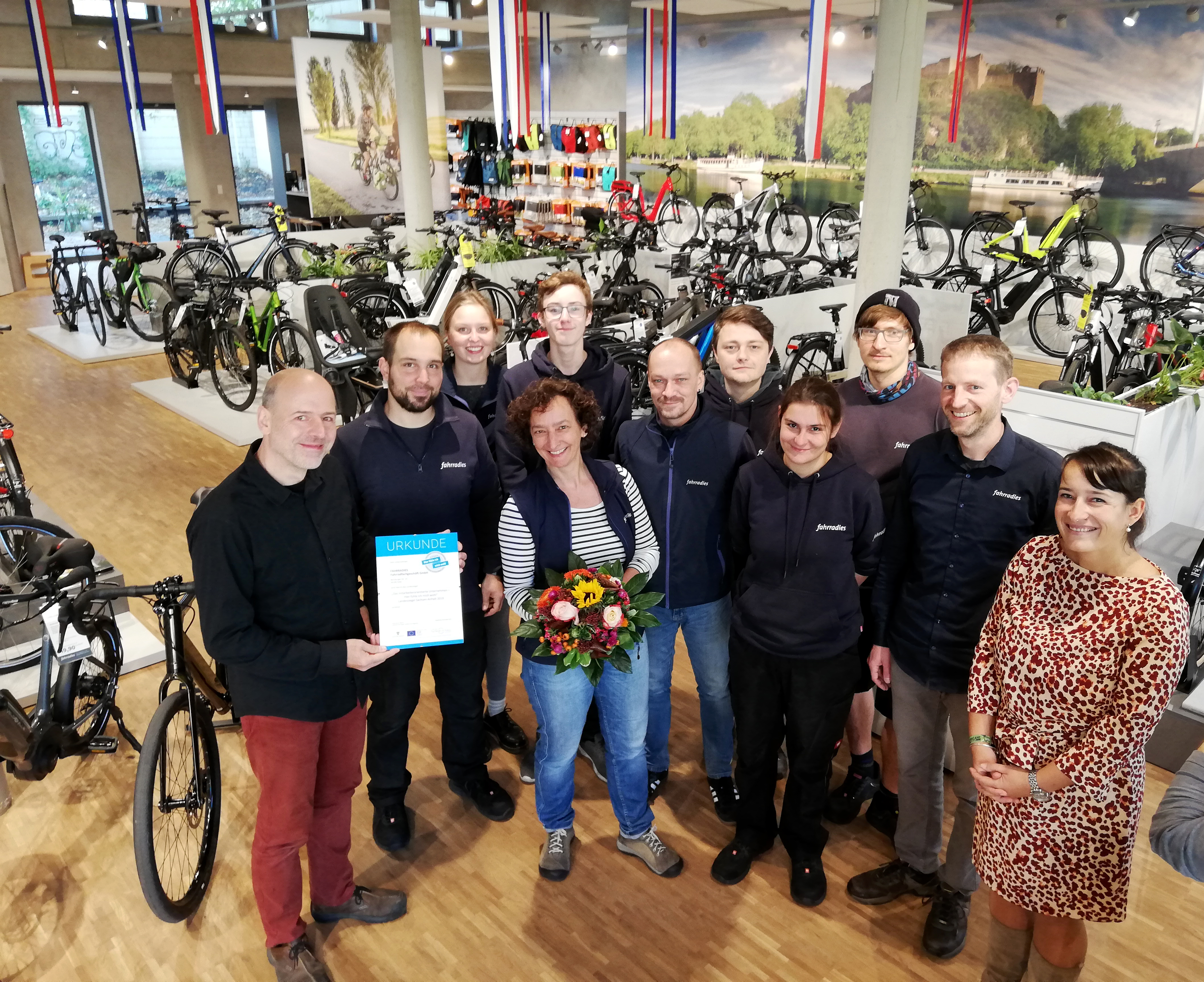 Viele Männer und Frauen vom Fahrradies schauen in die Kamera. Sie haben das Landessiegel als Urkunde und enen Blumenstrauß bekommen.