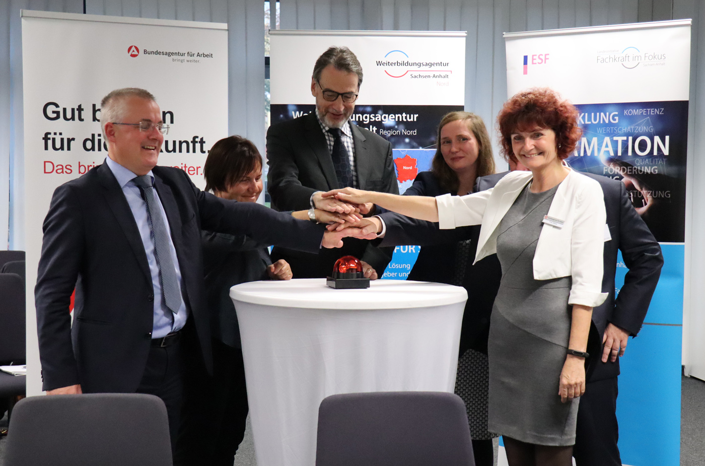 Sechs Personen halten ihre Hände über einem leuchtenden Buzzer.