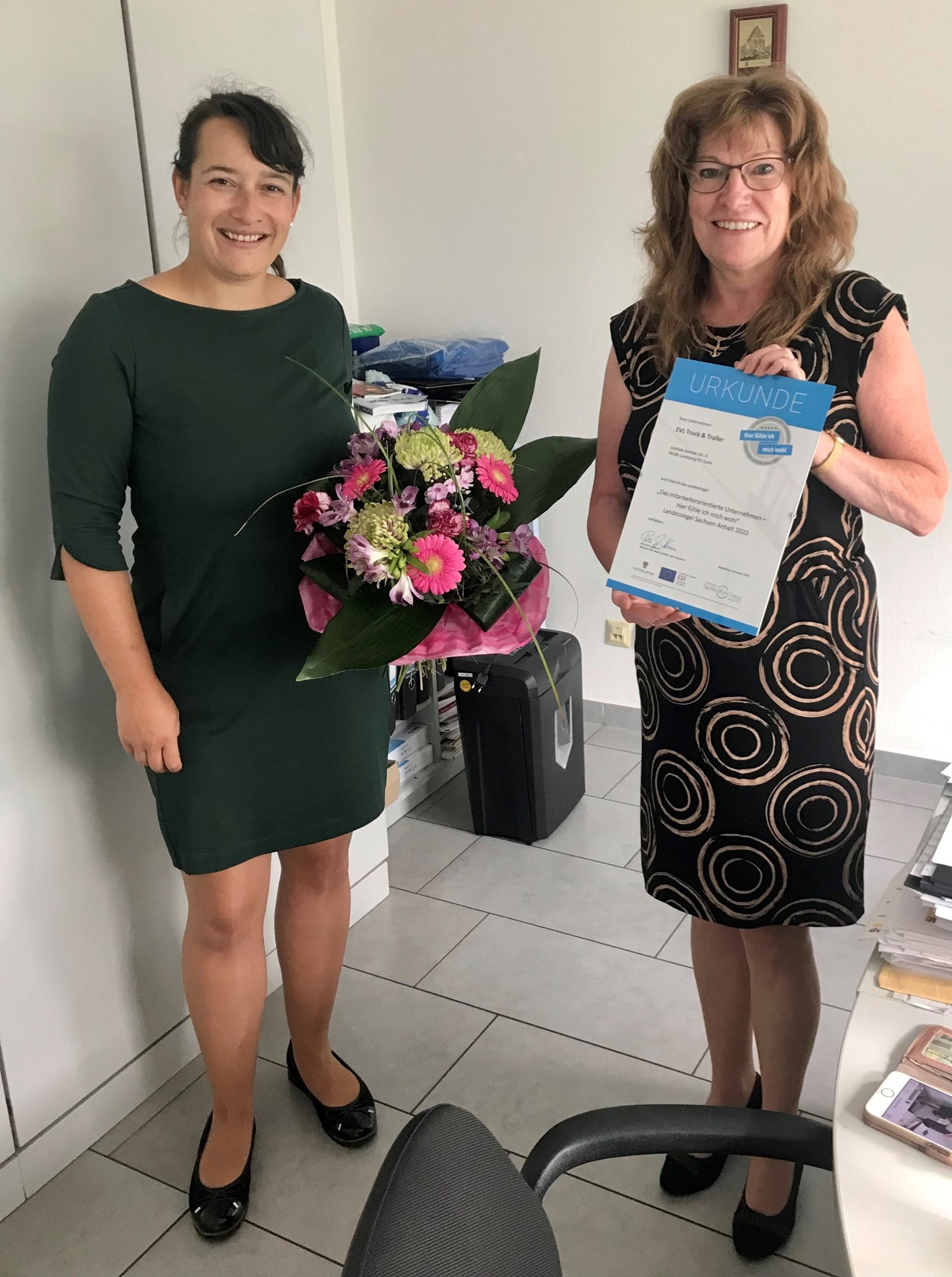 Regionalberaterin gibt Unternehmerin die Urkunde und einen Blumenstrauß
