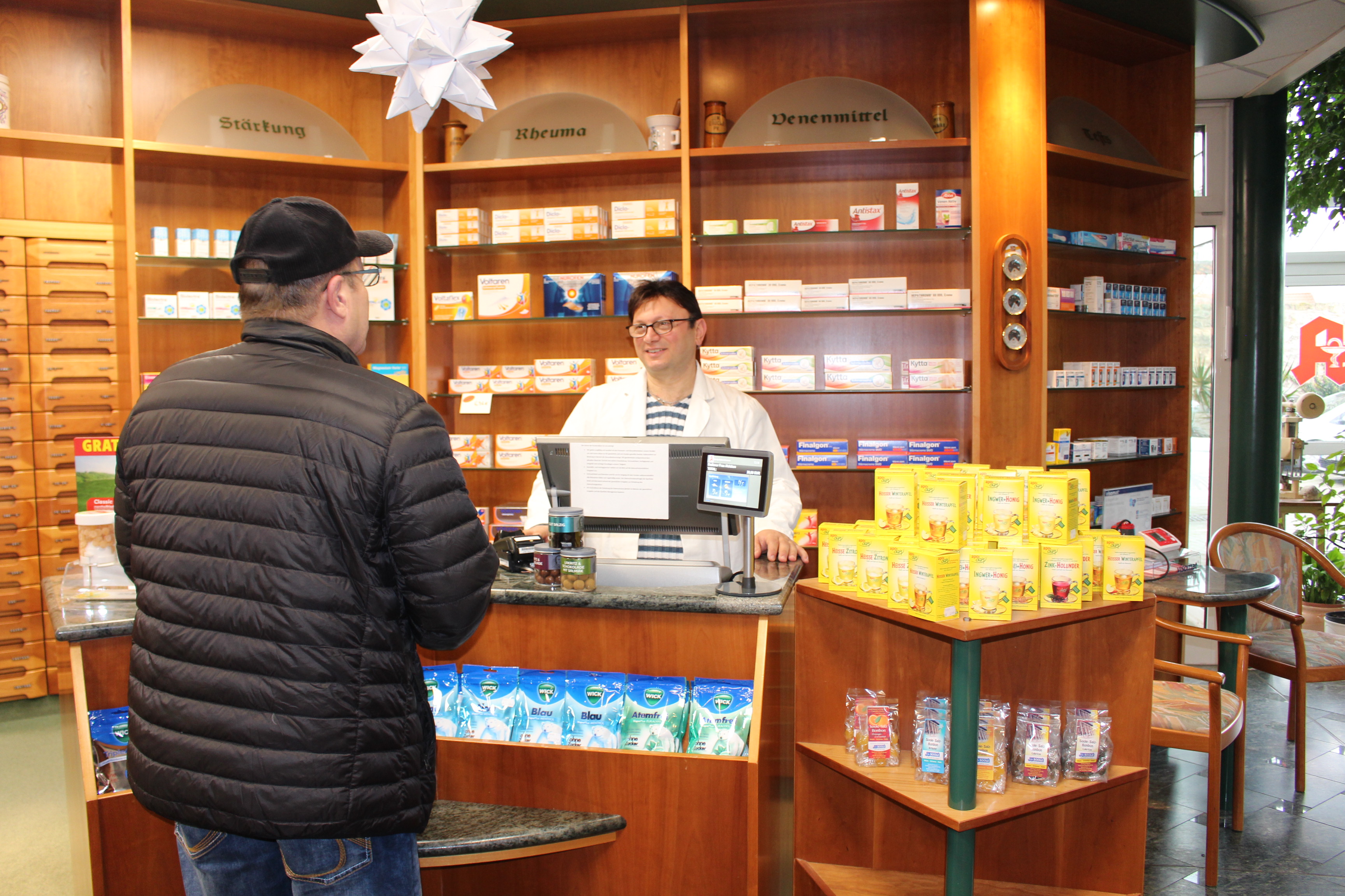 Wartan Wartanian steht hinter dem Tresen in einer Apotheke und bedient einen Kunden.